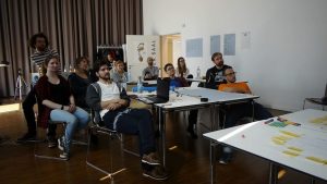Gruppe Menschen in Raum blickt in eine Richtung, Tisch mit Post its