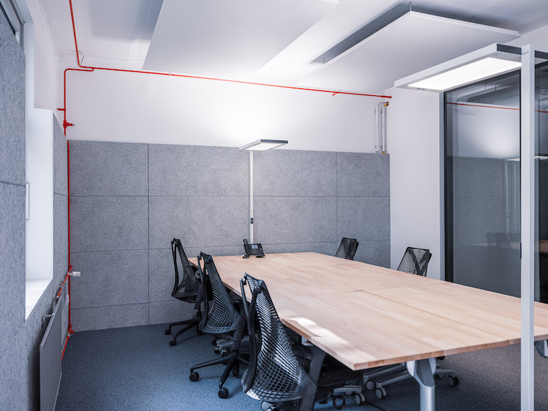 Büroraum hell beleuchtet mit grauen Wänden, Holztisch, fünf Bürostühlen und Telefon
