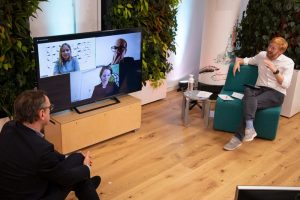 Zwei Männer vor Bildschirm mit Gesichtern von Menschen in Diskussion; Blog von Cradle to Cradle NGO
