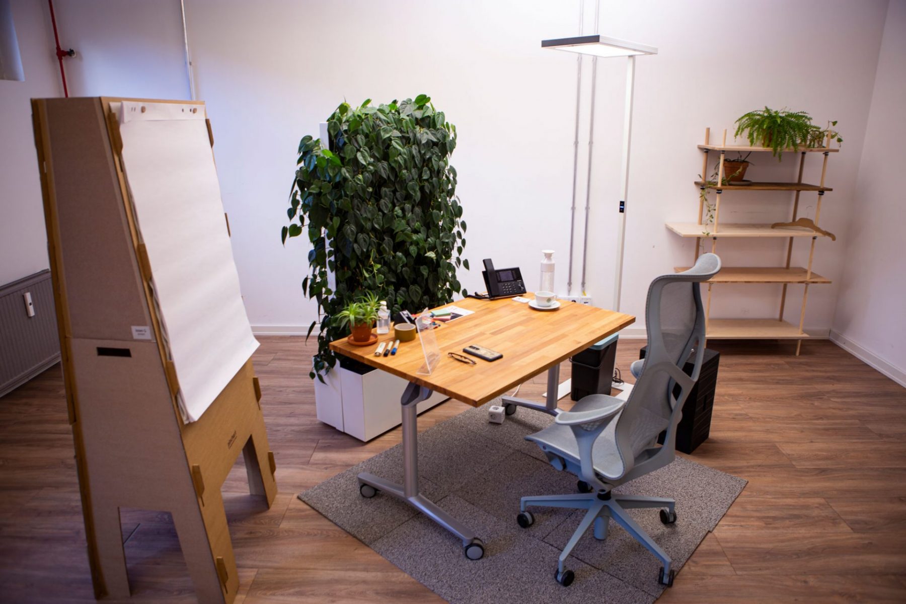 Ein Beispielbüro nach Cradle to Cradle: Tisch, Stuhl. Pflanzenwand, Whiteboard und diverse Büroprodukte auf dem Tisch liegend.