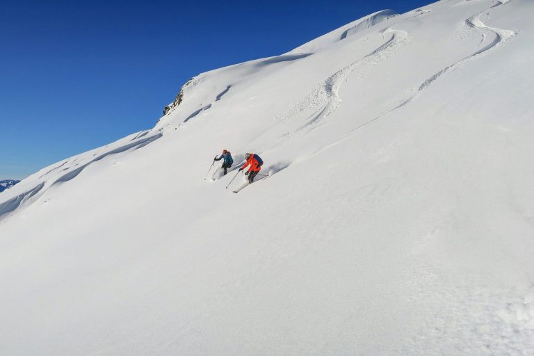 Zwei Personen fahren den Berg hinab und hinterlassen Spuren im Schnee