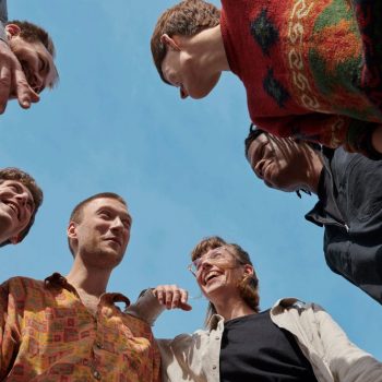 Gruppe junger Menschen, von unten fotografiert, blauer Himmel, im Kreis
