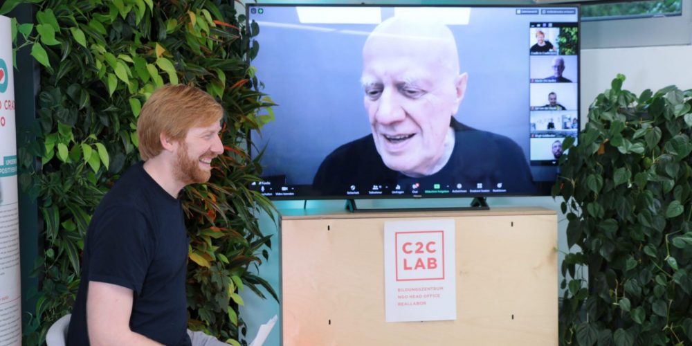 Tim Janßen sitzt auf Stuhl vor Bildschirm mit Gesicht von Ralf Fücks; Blog von Cradle to Cradle NGO