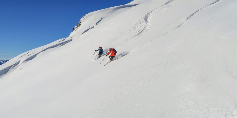 Zwei Personen fahren den Berg hinab und hinterlassen Spuren im Schnee